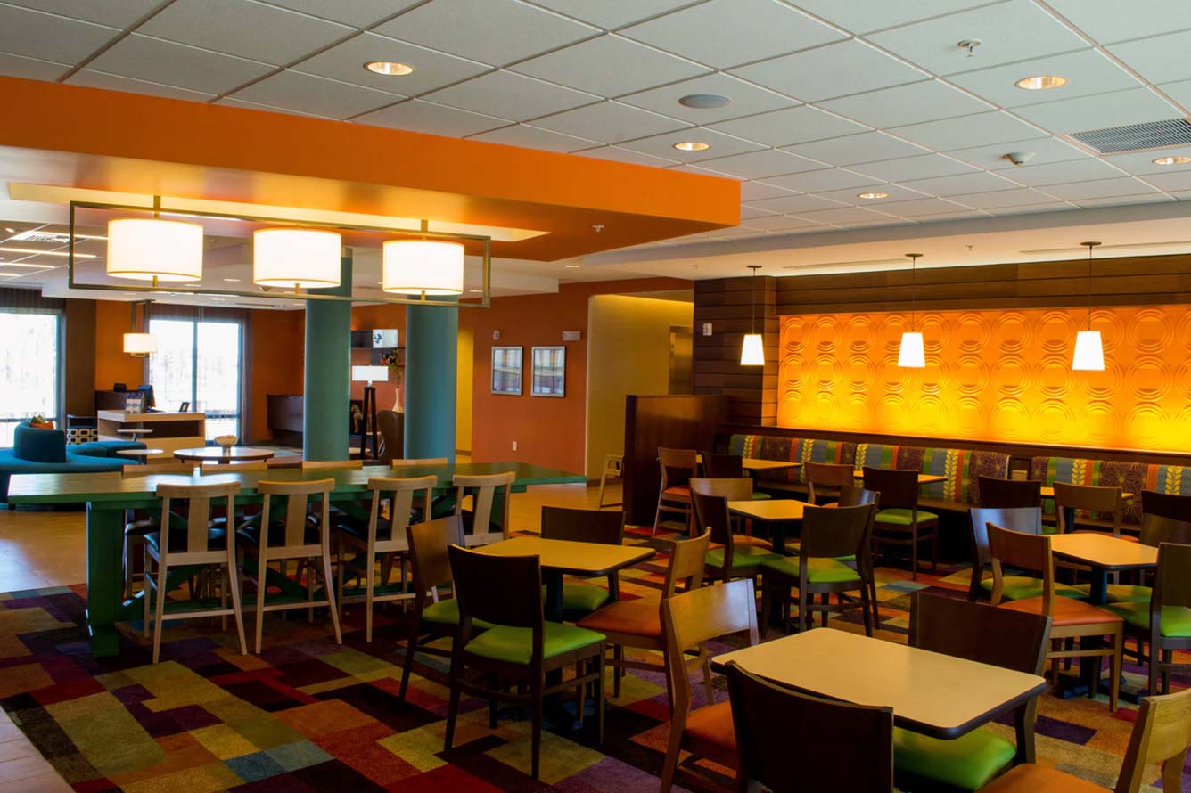 Modern Fort Walton Beach Hotel dining area with colorful chairs and warm orange wall lighting.