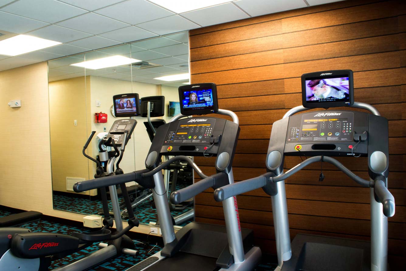Two treadmills with screens in a modern gym at Wavecrest Lodge, with mirror and wood panel wall.