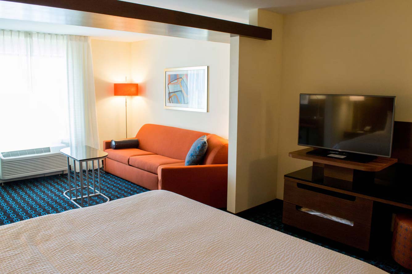 Relax in this Fort Walton Beach Hotel room with a bed, orange sofa, TV, and large window.