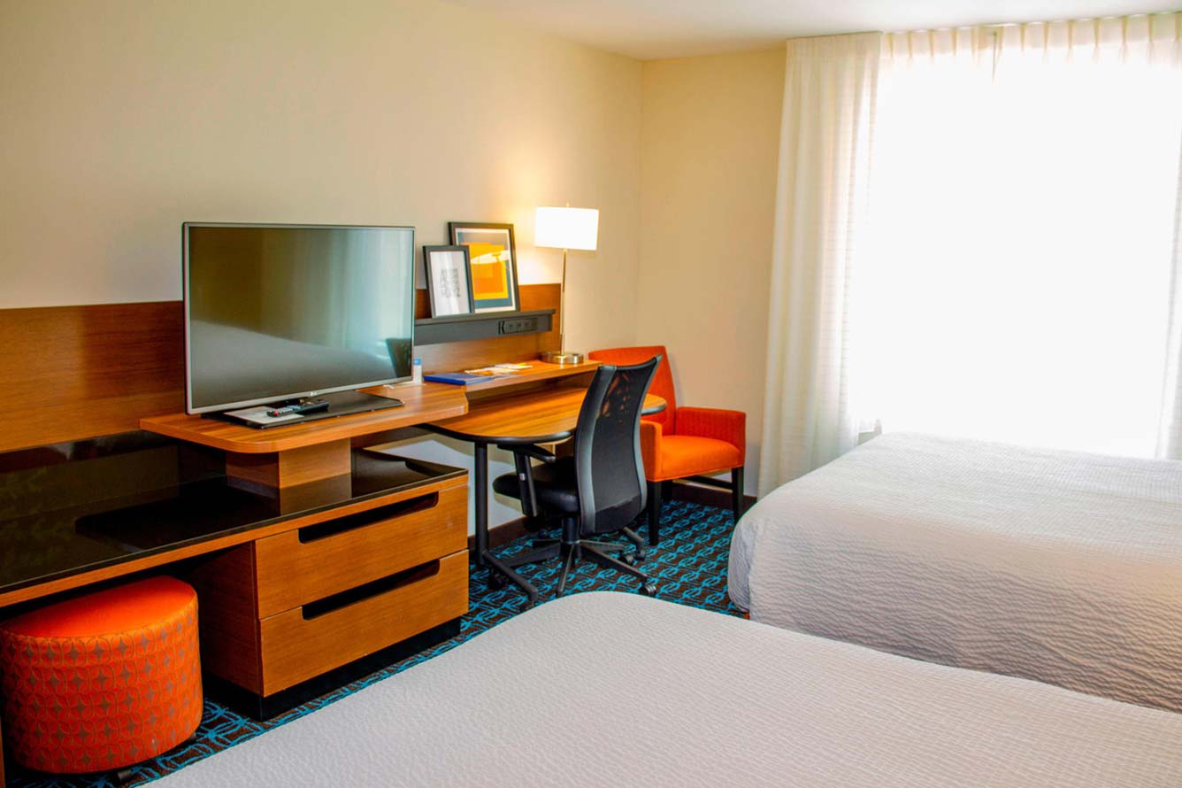 Hotel room at Wavecrest Lodge with two beds, desk, TV, orange chair, and large window.