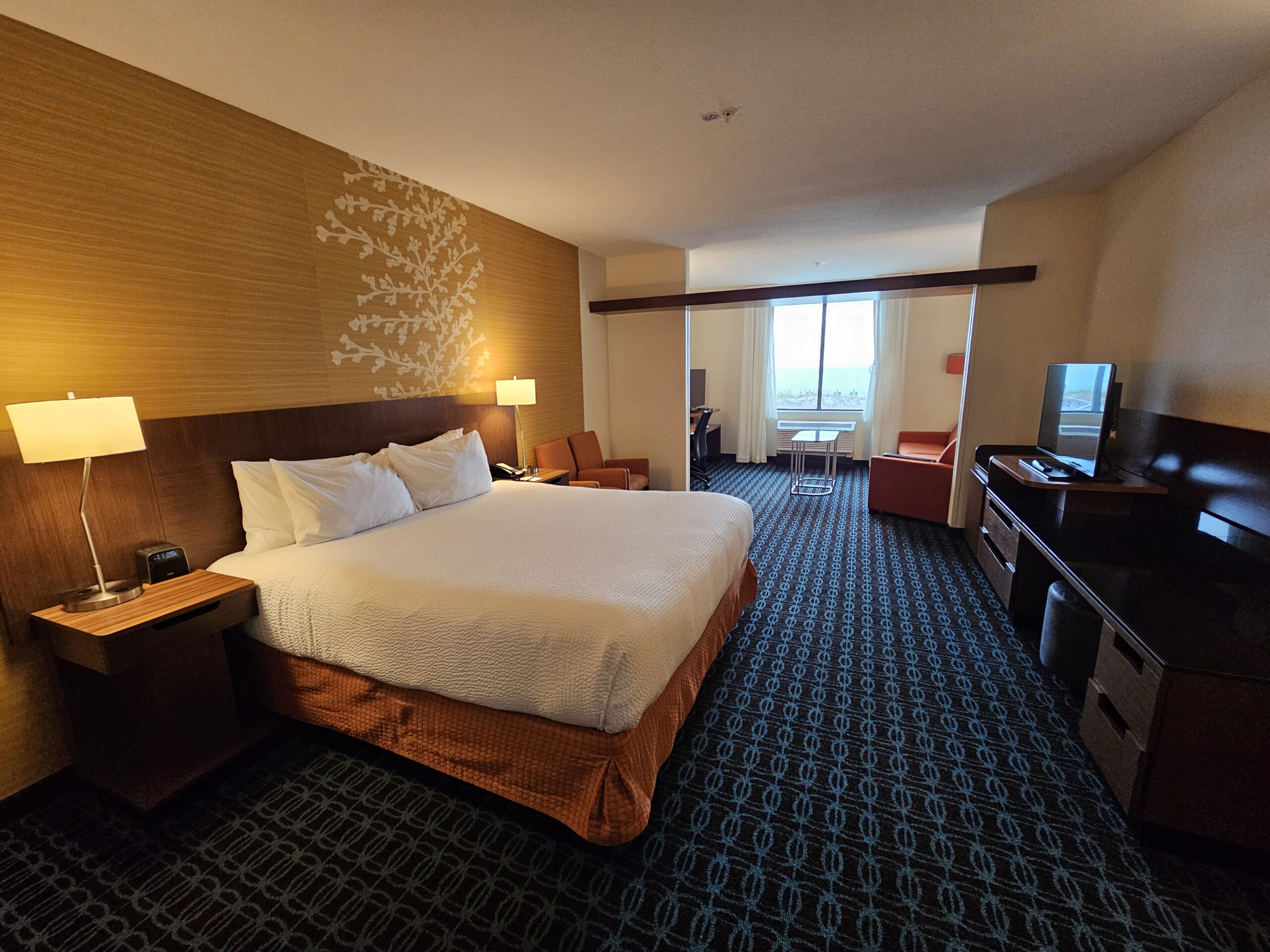 Wavecrest Lodge hotel room with king bed, desk, TV, armchairs, window, and warm lighting.
