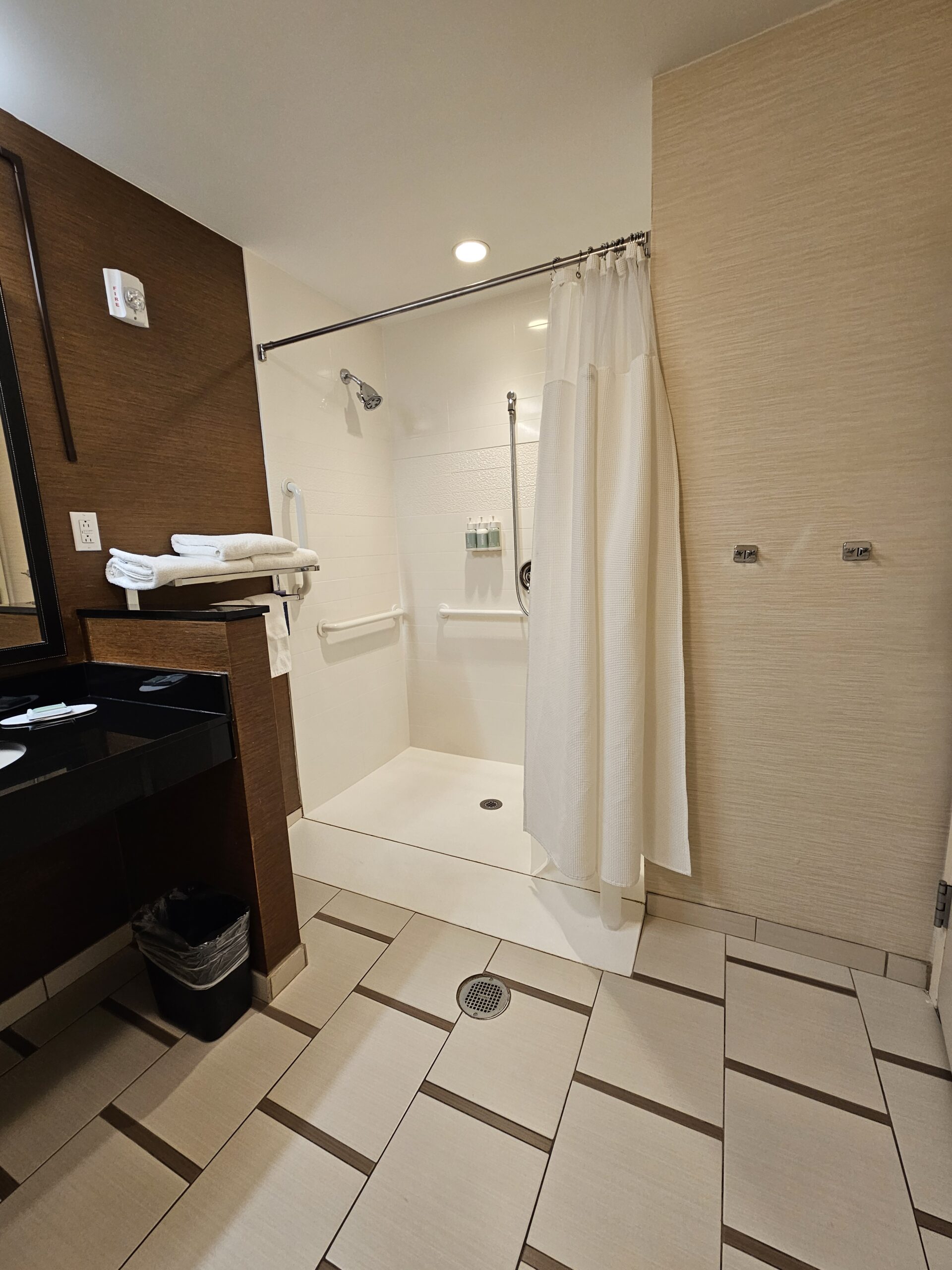 Accessible Wavecrest Lodge hotel bathroom with roll-in shower, grab bars, and folded towels on a shelf.