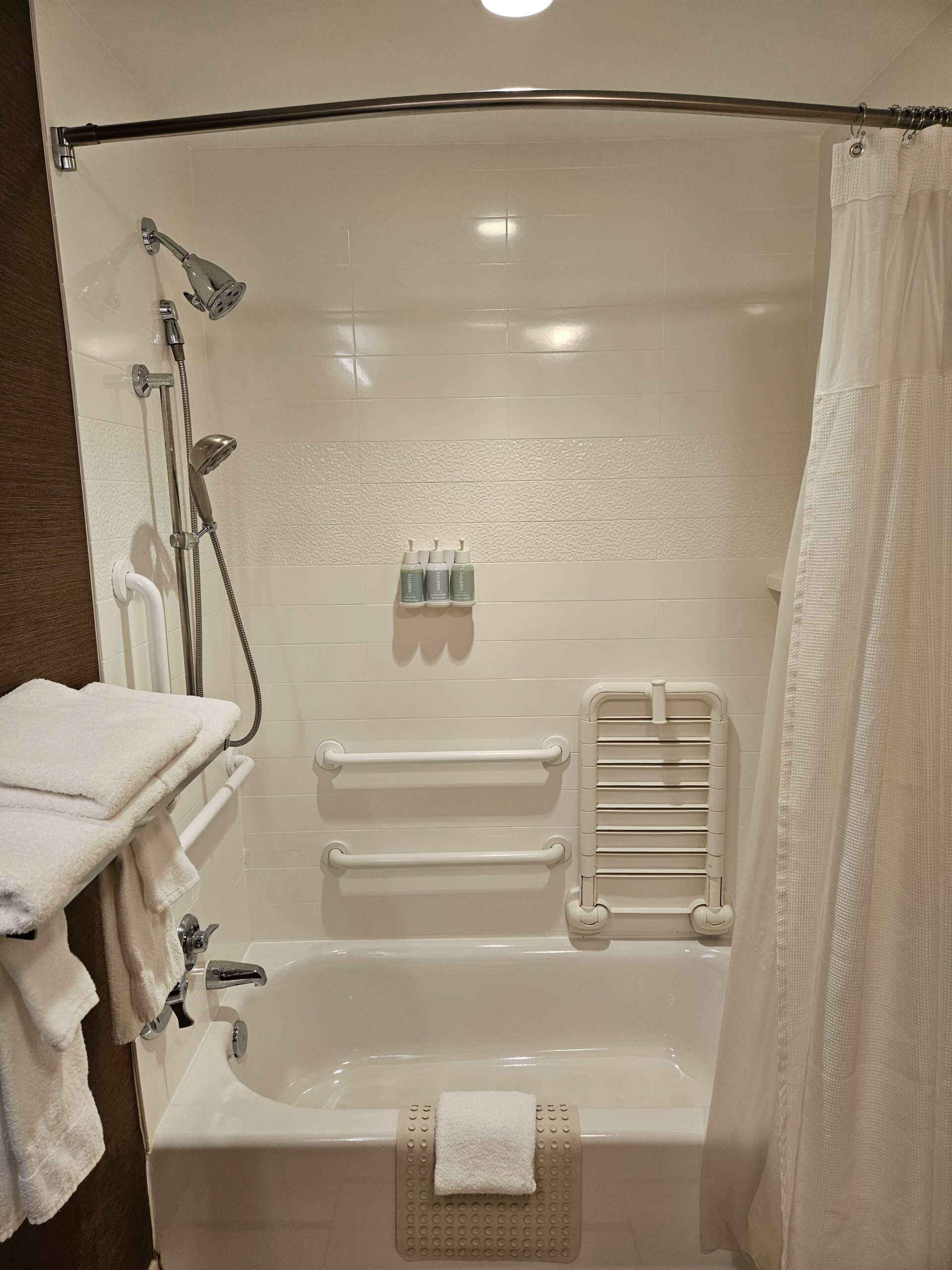 Accessible Wavecrest Lodge hotel bathtub with grab bars, shower, white towels, and curtain.