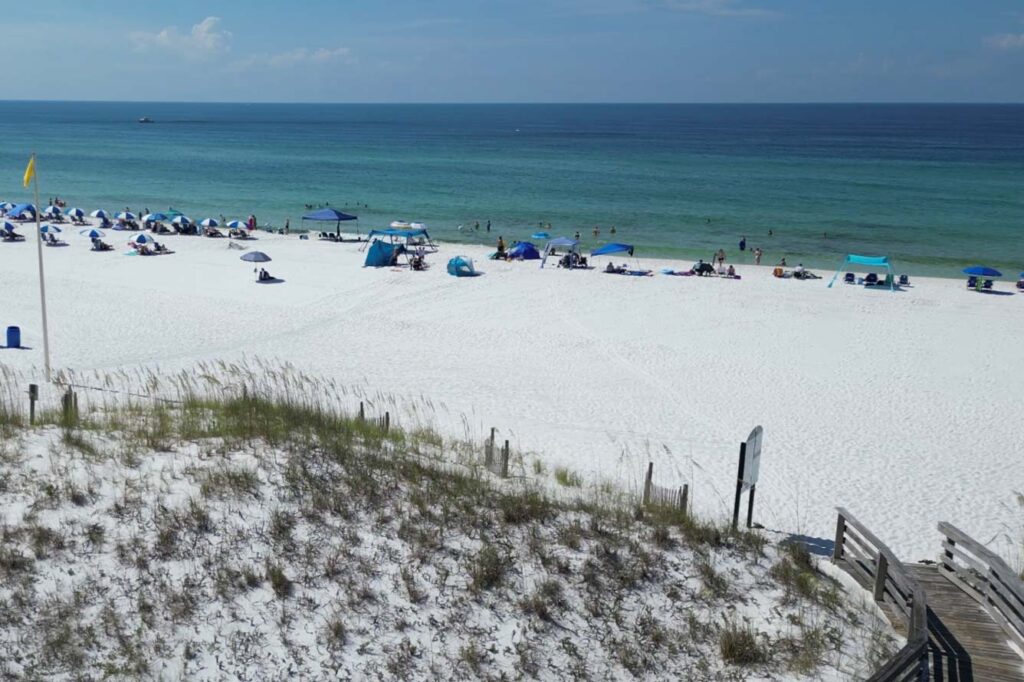 White sand beach with people, umbrellas, and ocean near Wavecrest Lodge under a clear sky.