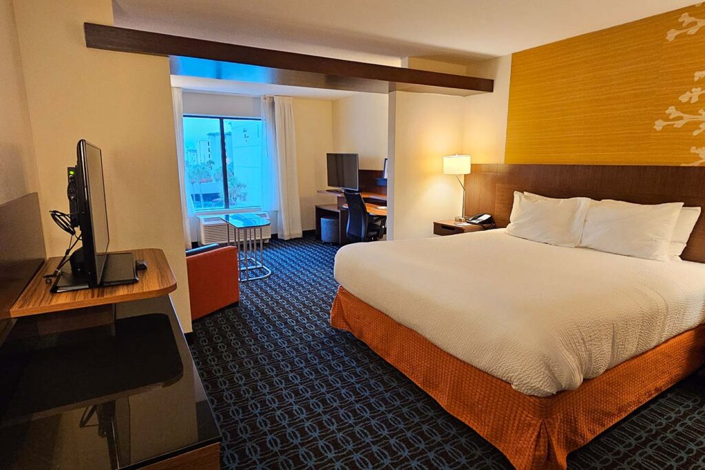Spacious Wavecrest Lodge hotel room with a large bed, TV, desk, chair, and bright window.