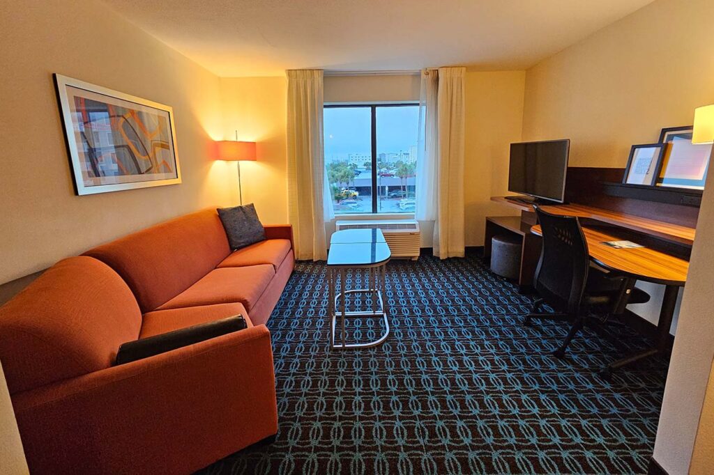 Wavecrest Lodge hotel room with red sofa, glass table, desk, TV, and city view window.