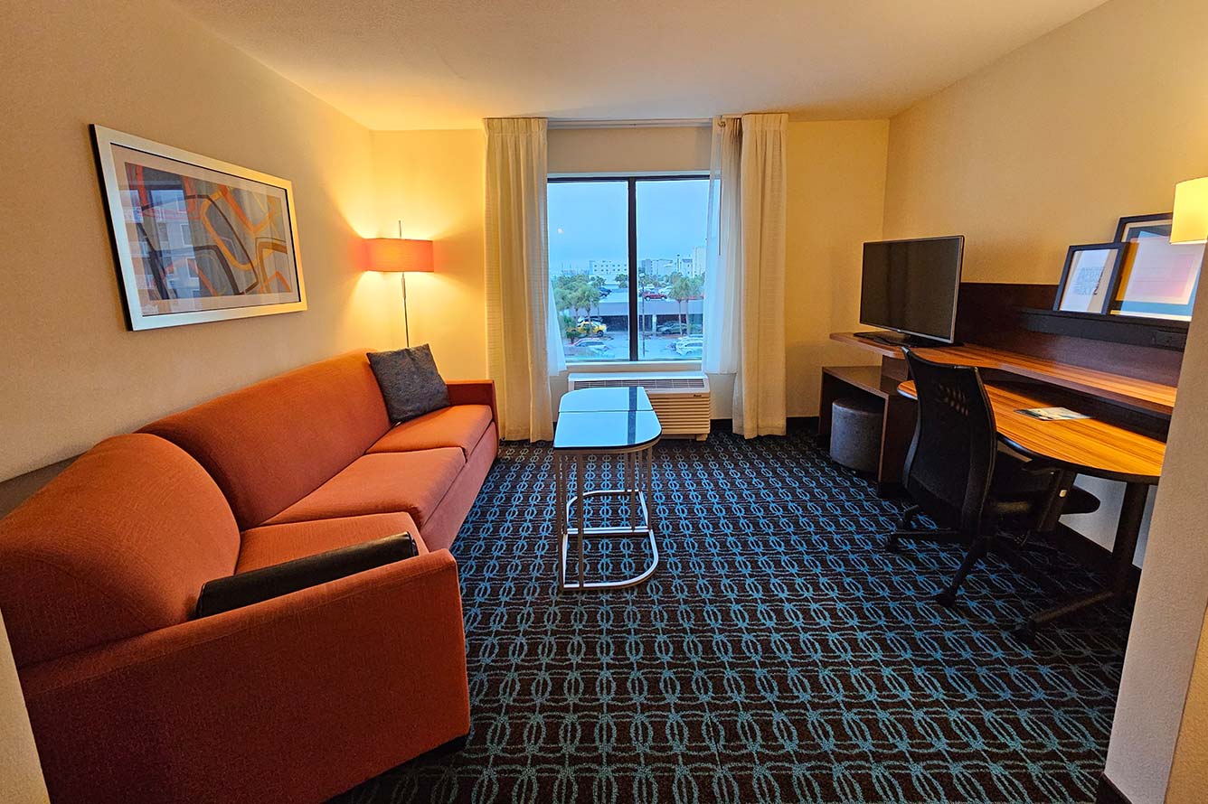 Wavecrest Lodge hotel room with red sofa, glass table, desk, TV, and city view window.