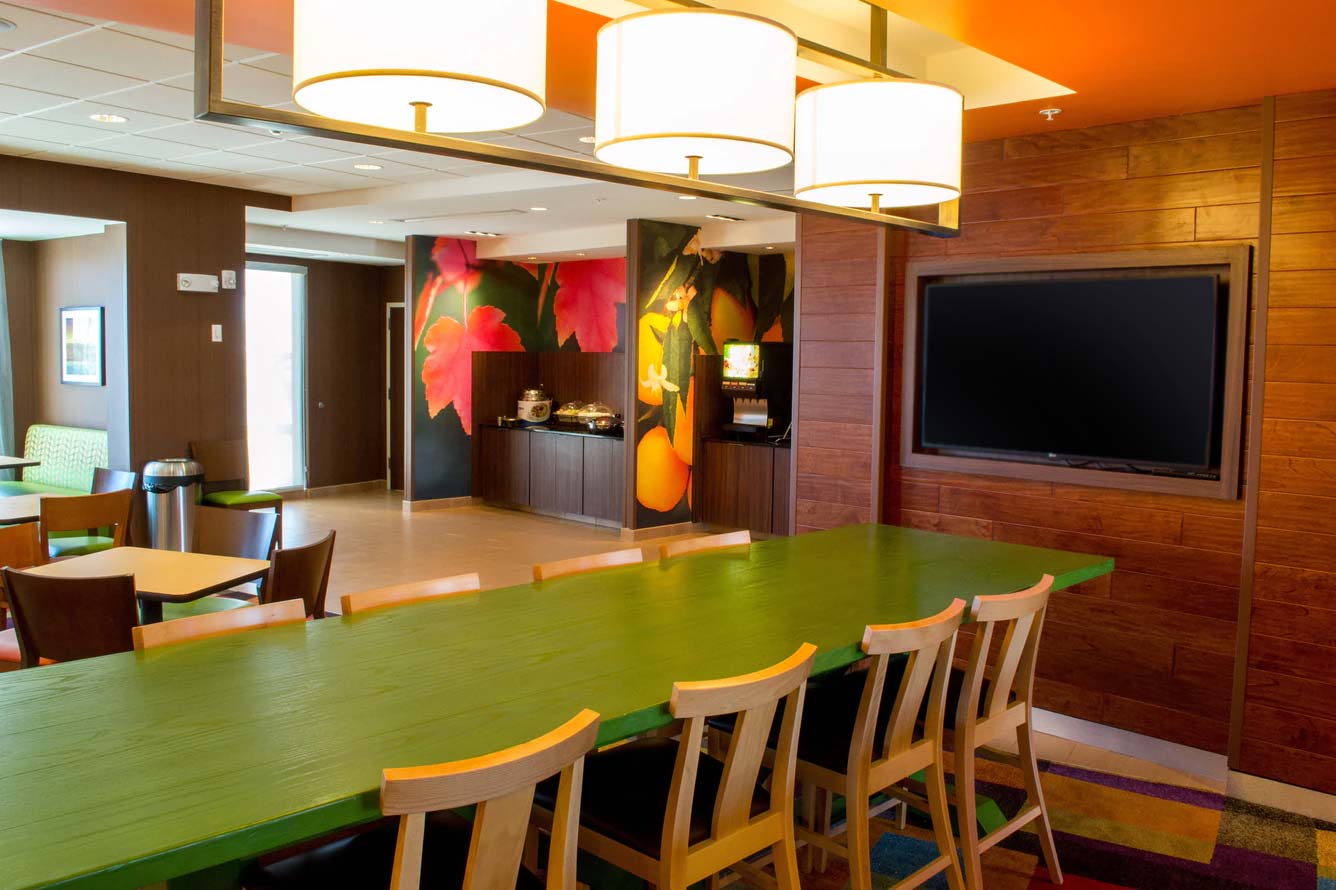 Modern dining area in Fort Walton Beach hotel with green table, wooden chairs, and breakfast counter.