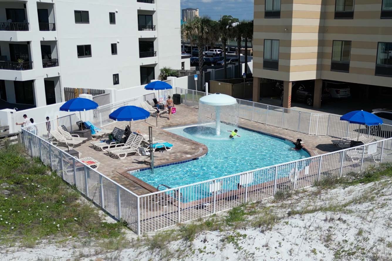 A fenced outdoor pool at Wavecrest Lodge with blue umbrellas, lounge chairs, and swimmers.