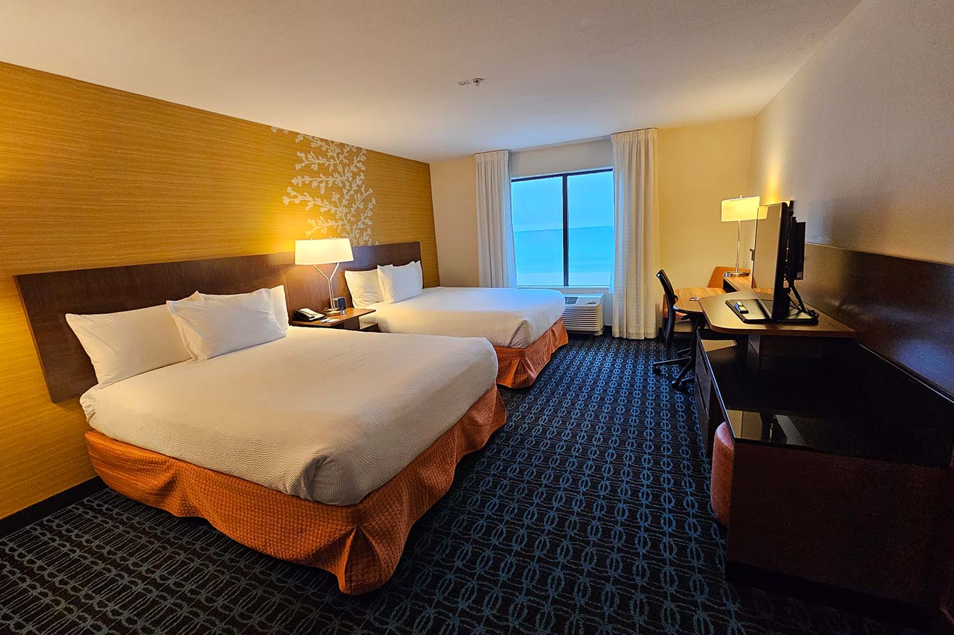 Hotel room with two beds, desk, TV, and window at Wavecrest Lodge in Fort Walton Beach.