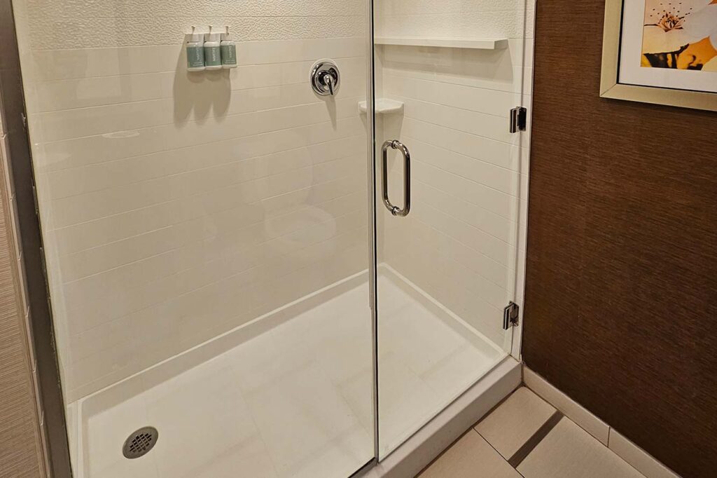 White walk-in shower with glass door, wall-mounted soaps, and chrome handle at Wavecrest Lodge.