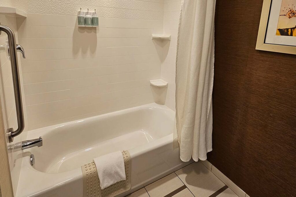 White bathtub with shower curtain and grab bar in a clean Fort Walton Beach Hotel bathroom.
