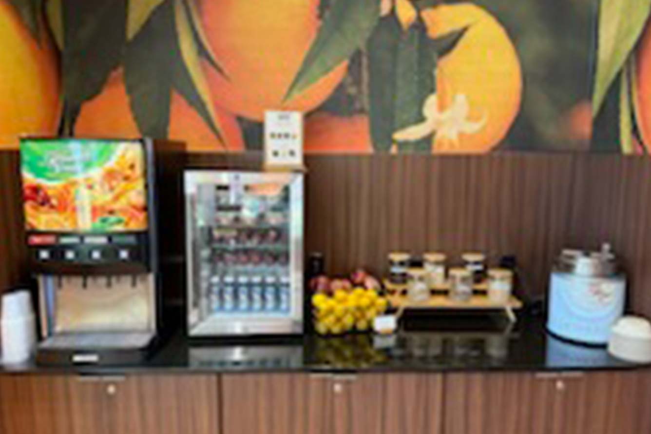 Wavecrest Lodge hotel breakfast station with juice machine, mini fridge, fruit, and cereal dispenser.