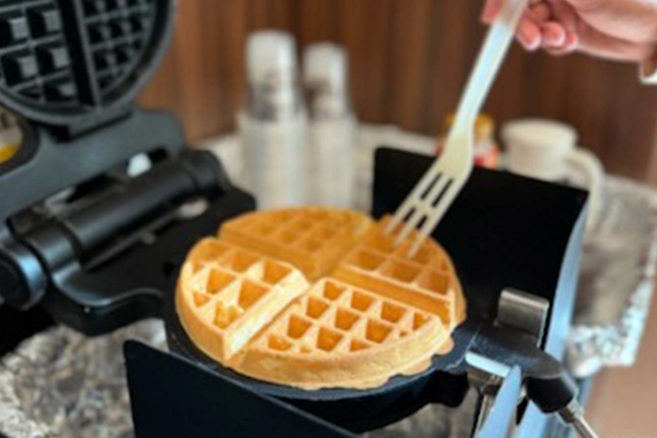 A hand uses a fork to lift a waffle from a waffle maker at a Fort Walton Beach Hotel.