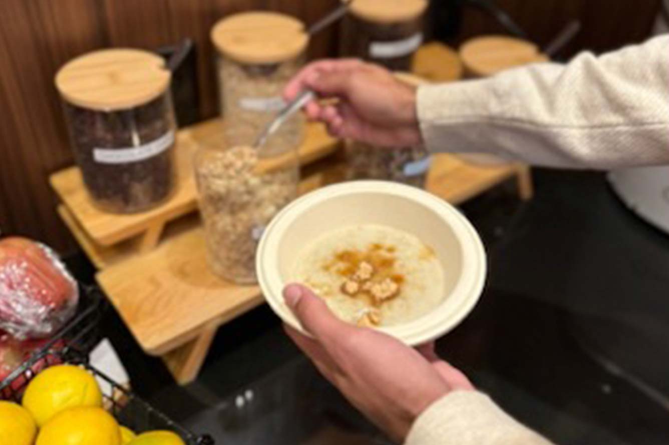 Person scooping granola at Wavecrest Lodge near jars of toppings and a basket of fresh fruit.