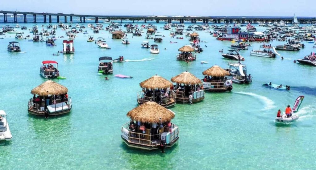 Crab Island near Destin is a popular boating destination where visitors gather in shallow emerald water to swim, relax, and enjoy floating tiki huts along the Emerald Coast.