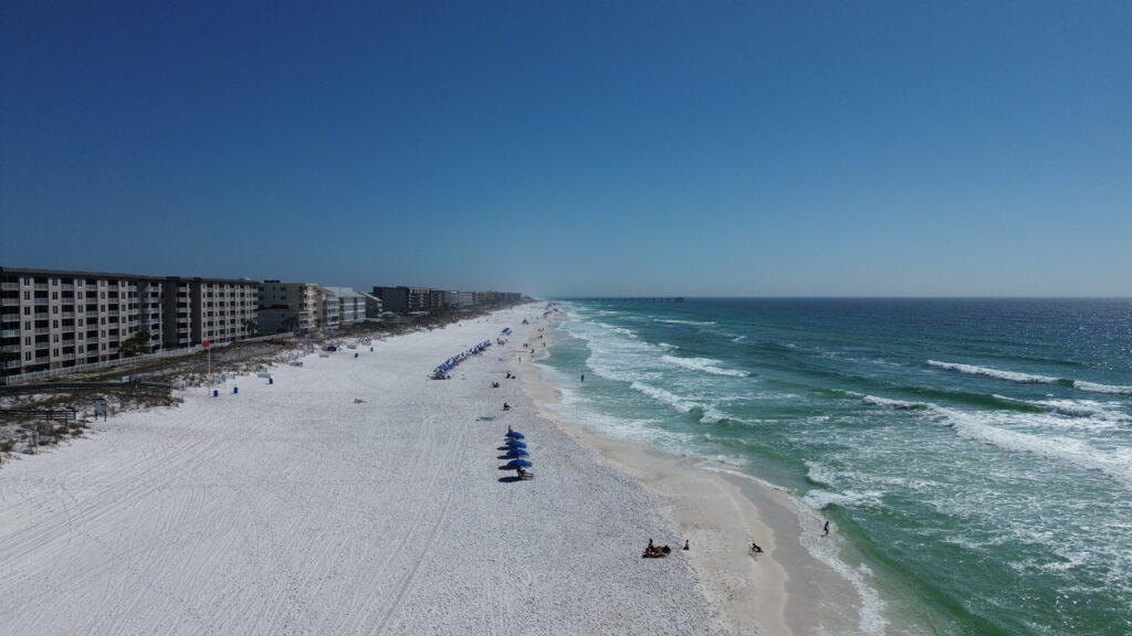 Aerial view of the beach in front of Wavecrest Lodge on Okaloosa Island with white sand and emerald waters along Florida’s Emerald Coast near Fort Walton Beach.