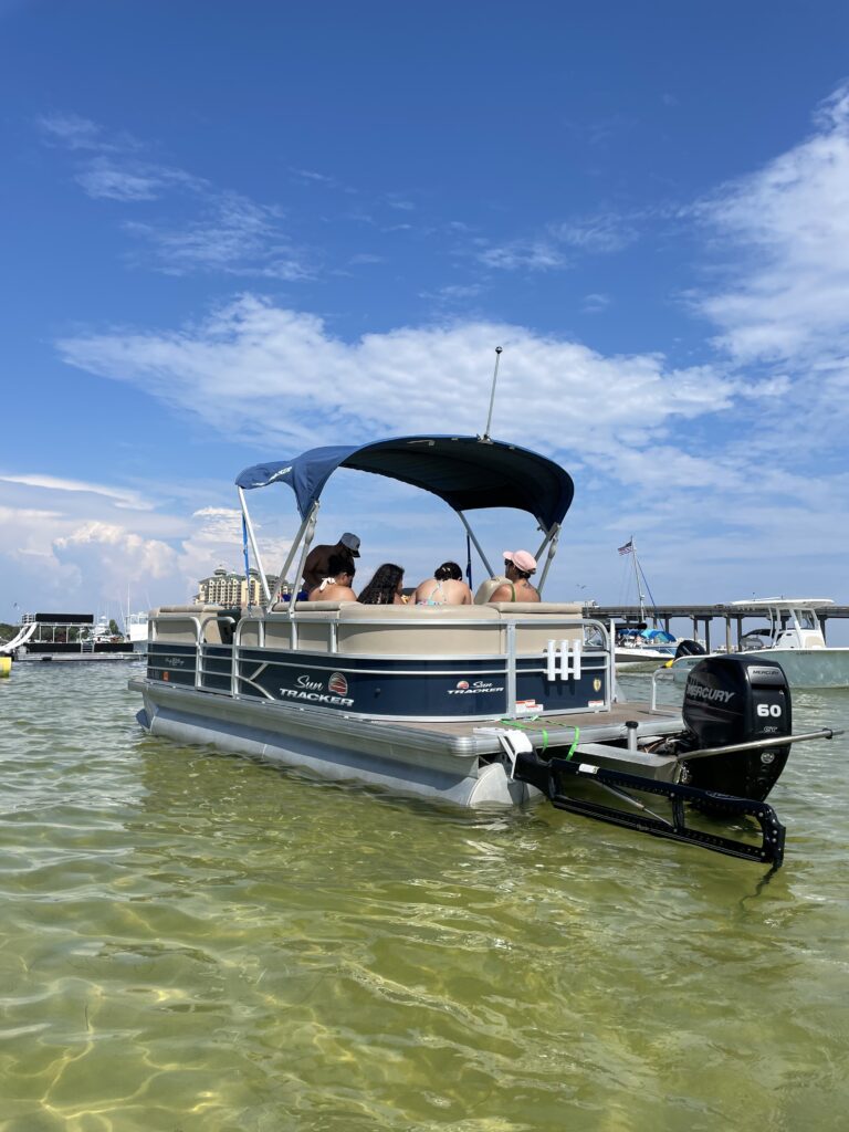 Pontoon boat with passengers anchored in shallow emerald water near Crab Island in Destin, Florida on the Emerald Coast.
