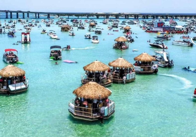 Crab Island near Destin is a popular boating destination where visitors gather in shallow emerald water to swim, relax, and enjoy floating tiki huts along the Emerald Coast.