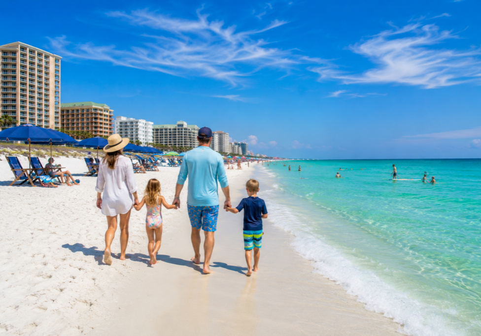 Family-friendly summer beach on Okaloosa Island with white sand beaches, emerald water, and beachfront hotels along the Emerald Coast
